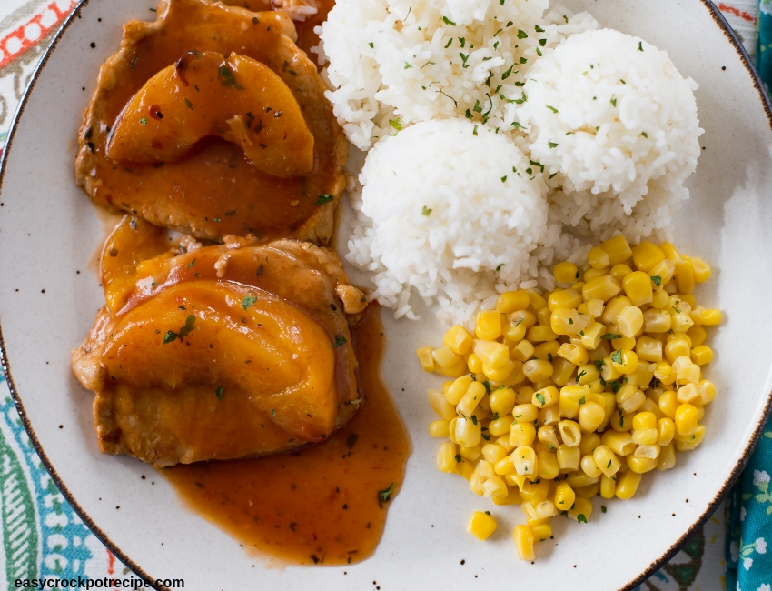 Spicy Peach Boneless Pork Chops on a glass plate served with cooked white rice and corn kernals.