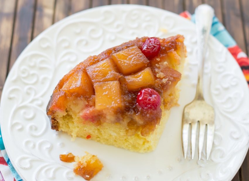 A slice of Crock Pot Pineapple Upside Down Cake on a white plate with a colorful napkin behind it.