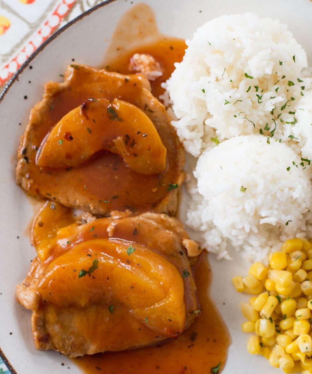 Peach Pork Chops served with rice and corn on a dinner plate.