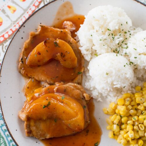 Peach Pork Chops served with rice and corn on a dinner plate.