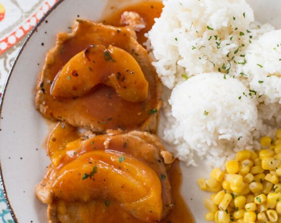 Peach Pork Chops served with rice and corn on a dinner plate.