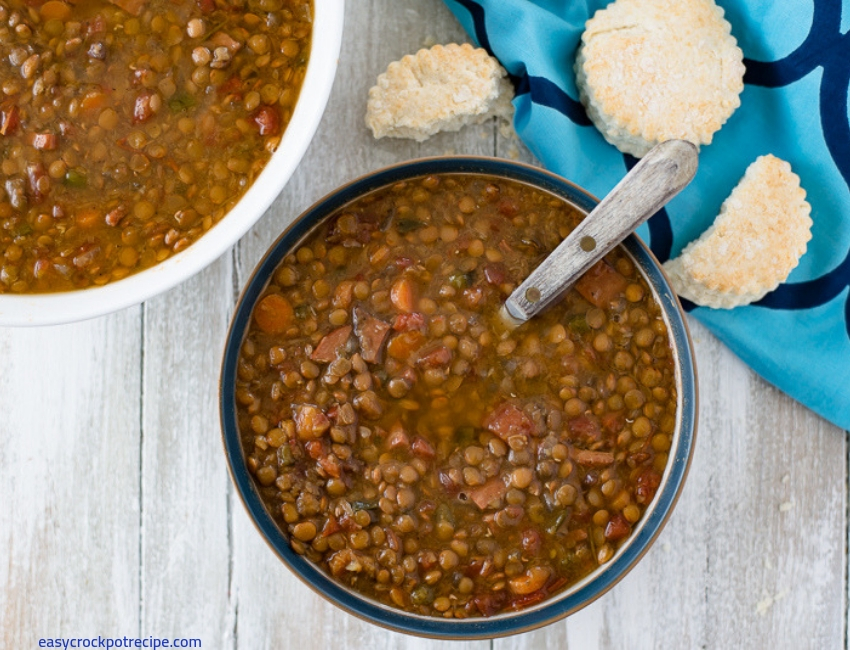 A big bowl filled with a serving of Crock Pot Ham and Lentils Soup served with biscuits. 