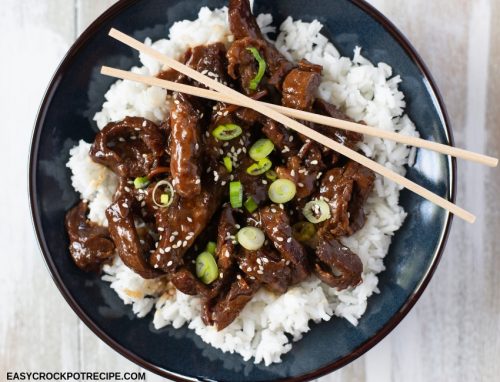 a dark blue bowl filled with tender Crock Pot Mongolian Beef served over a bed of cooked white rice with sliced green onions as the garnish.