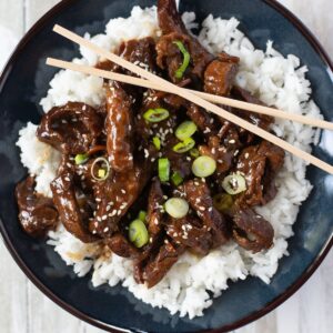 Blue bowl filled with tender Mongolian Beef served over white rice.