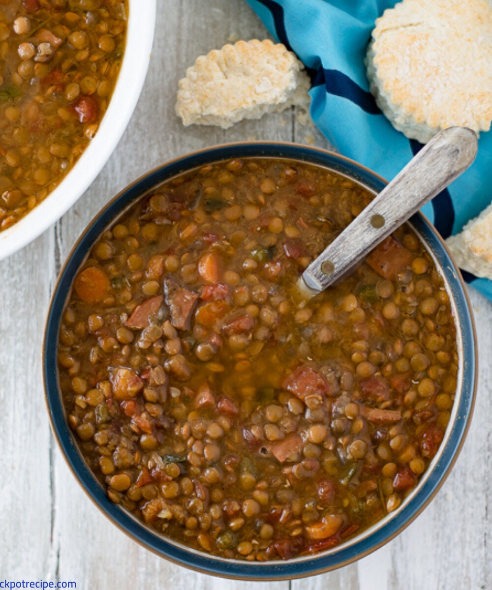 a bowl filled with Crock Pot Ham and Lentils soup with a plate of biscuits in the background.