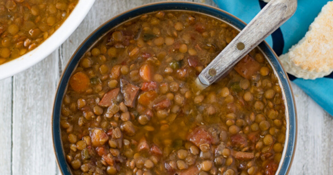 a bowl filled with Crock Pot Ham and Lentils soup with a plate of biscuits in the background.