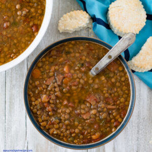 a bowl filled with Crock Pot Ham and Lentils soup with a plate of biscuits in the background.