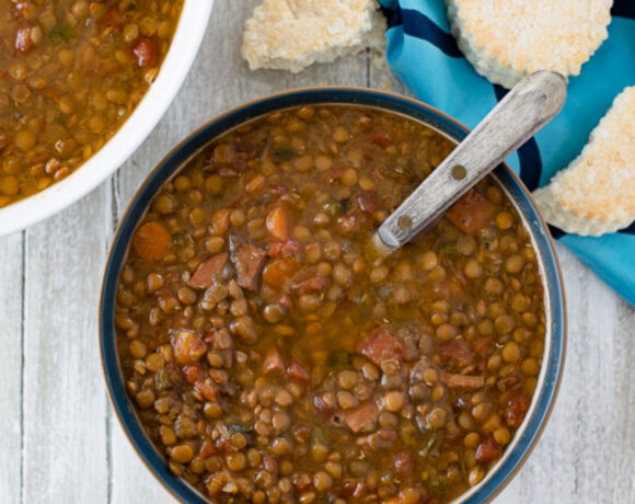 a bowl filled with Crock Pot Ham and Lentils soup with a plate of biscuits in the background.