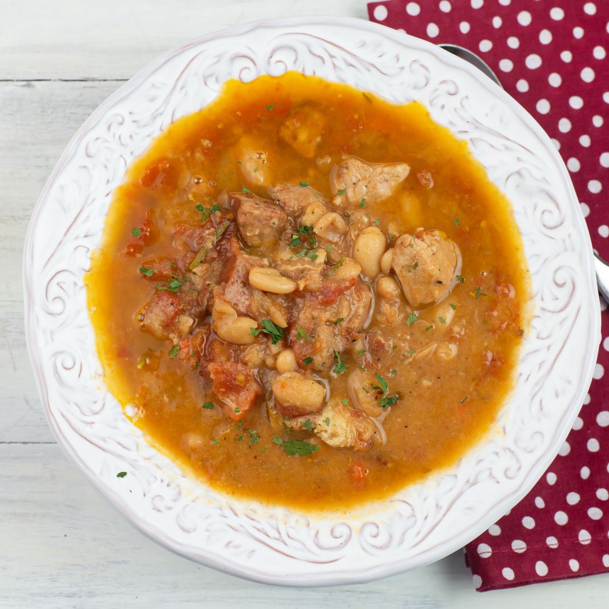 Crockpot Pork and white bean Cassoulet in a white bowl with a cloth napkin in the background.