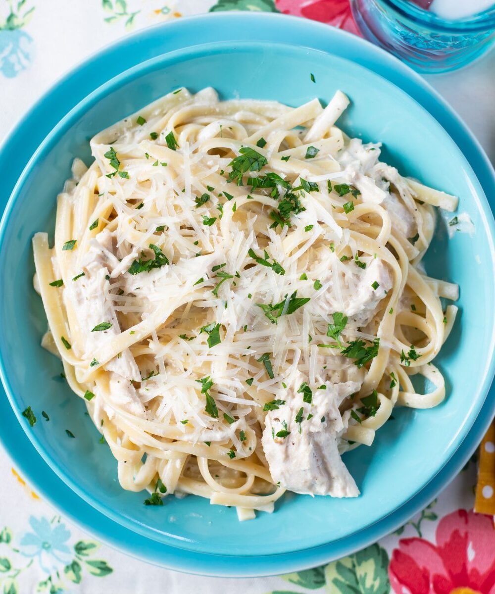 Serving Crock Pot Chicken Alfredo in a blue bowl on placemat.