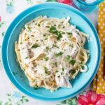 Serving Crock Pot Chicken Alfredo in a blue bowl on placemat.